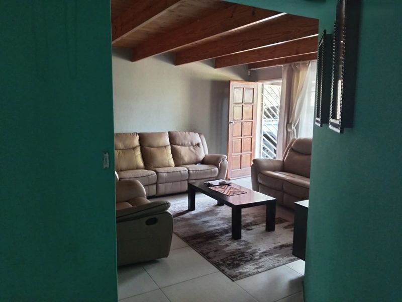A living room featuring exposed timber ceiling beams, tiled flooring, and direct access to an exterior door.