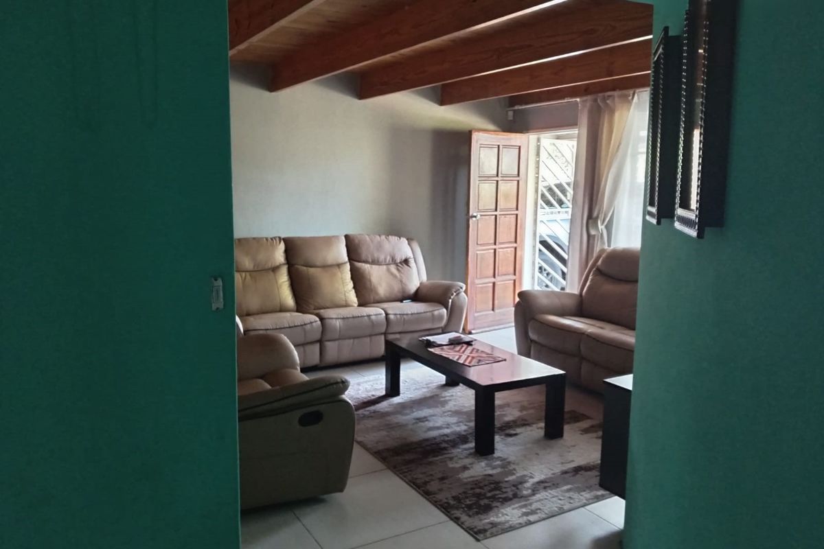 A living room featuring exposed timber ceiling beams, tiled flooring, and direct access to an exterior door.