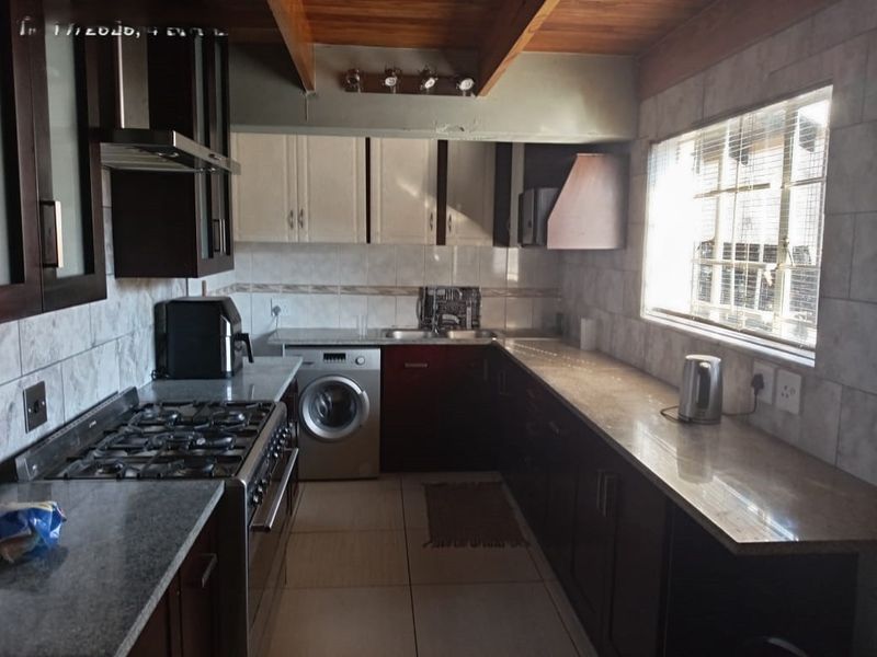 A functional kitchen featuring dark and light cabinetry, stone countertops, a gas stove with extractor, and exposed timber ceiling beams.