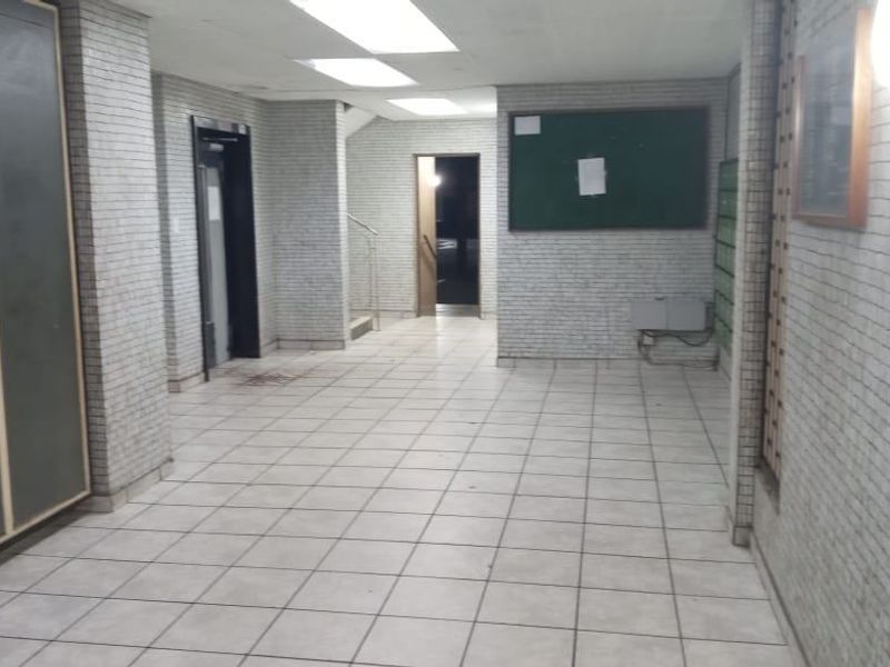 A communal apartment building hallway featuring tiled flooring, wall cladding, an elevator, and built-in mailboxes in a dated condition.
