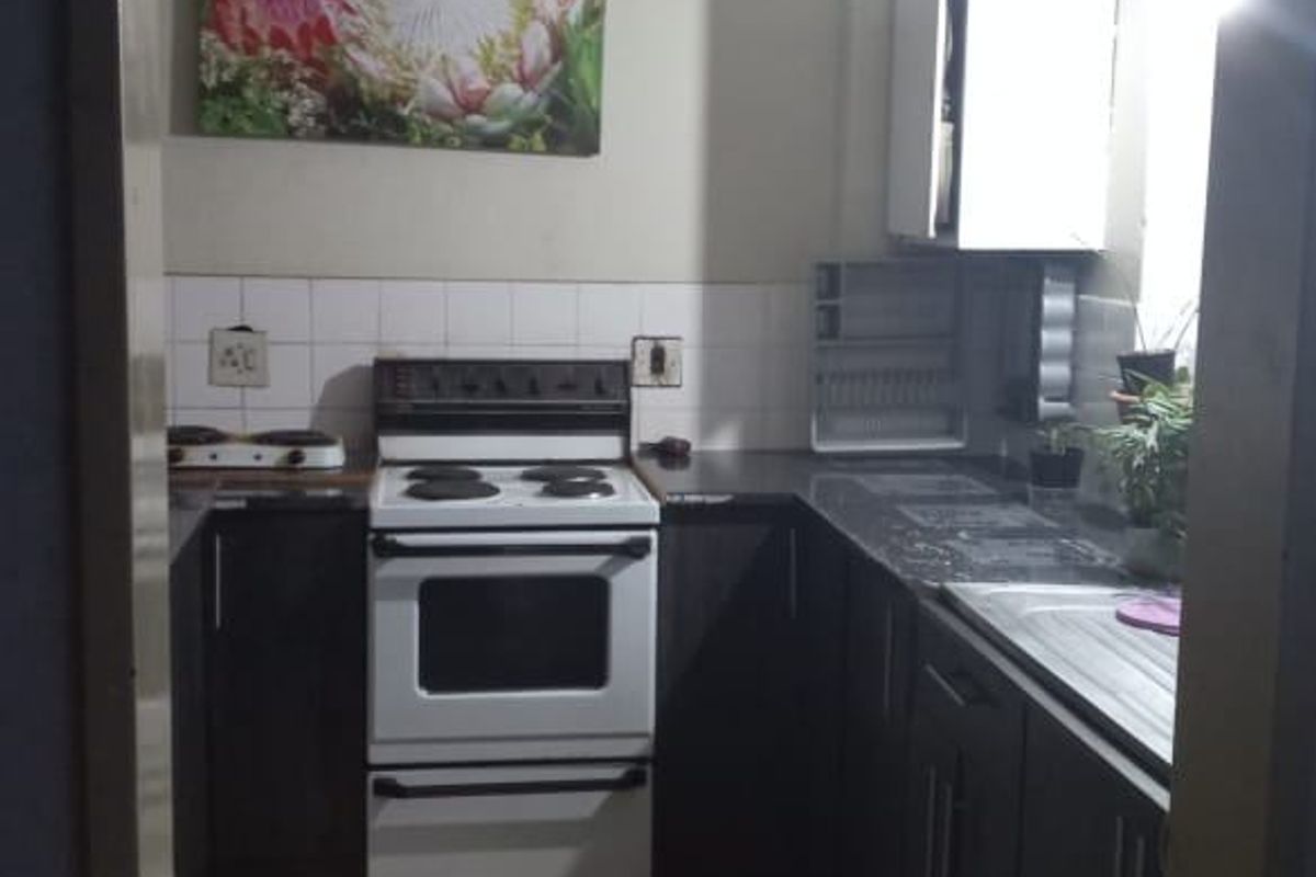 A functional U-shaped kitchen featuring dark cabinetry, a freestanding stove, tiled backsplash, and laminate countertops.