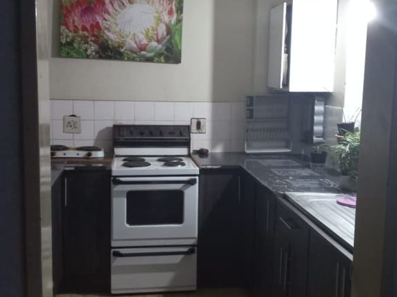 A functional U-shaped kitchen featuring dark cabinetry, a freestanding stove, tiled backsplash, and laminate countertops.