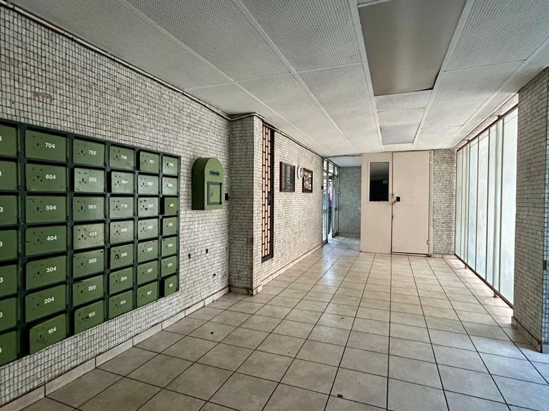 A communal apartment building entrance lobby featuring tiled flooring, mosaic wall tiling, and a bank of built-in mailboxes.