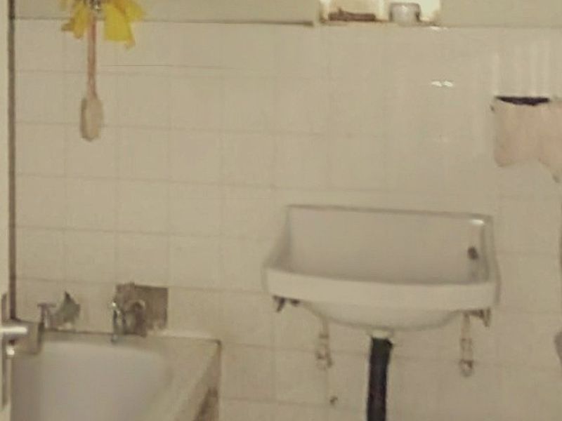 A dated bathroom featuring a bathtub, wall-mounted basin, and recessed storage niche, requiring significant renovation and modernization of fixtures and finishes.