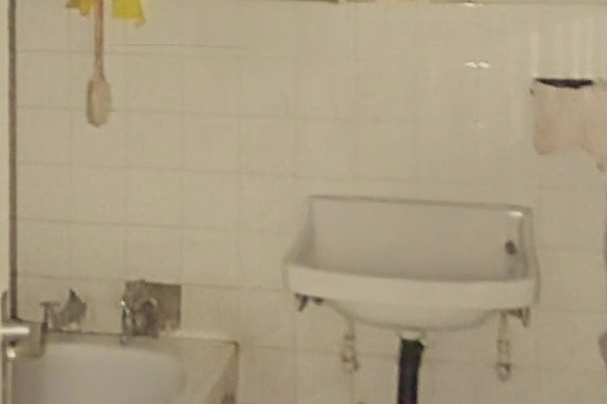 A dated bathroom featuring a bathtub, wall-mounted basin, and recessed storage niche, requiring significant renovation and modernization of fixtures and finishes.
