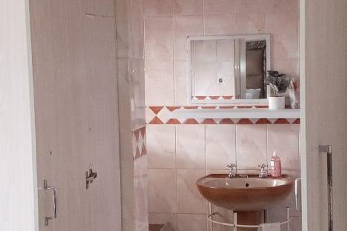 A compact bathroom featuring a pedestal sink, tiled walls with decorative border, and tiled flooring, accessed through a doorway with built-in cabinetry.