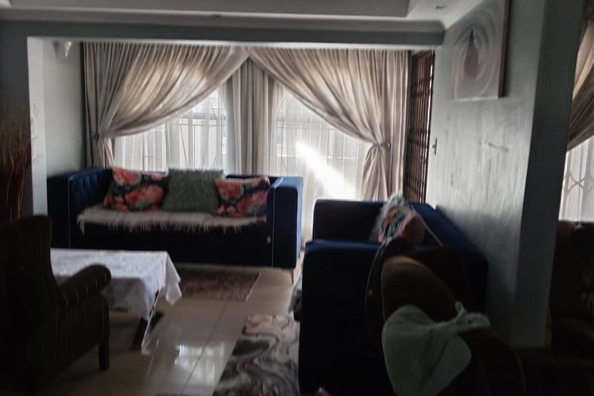 A comfortable living room featuring tiled flooring, recessed ceiling lighting, and large windows dressed with floor-to-ceiling curtains.