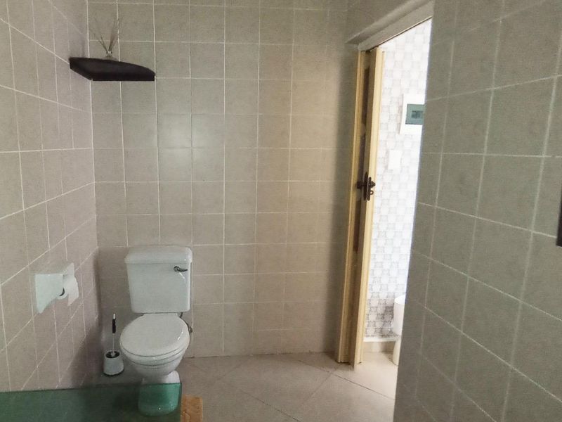 A functional bathroom featuring neutral ceramic wall and floor tiling, equipped with a standard toilet and built-in glass shelving.