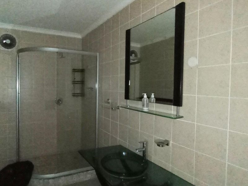 A functional bathroom featuring a glass shower enclosure, a modern vessel sink with a glass vanity shelf, and neutral wall tiling.