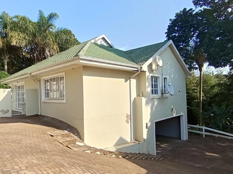 Exterior view of a townhouse featuring a tiled roof, paved driveway, and integrated garage with visible signs of exterior wall maintenance required.