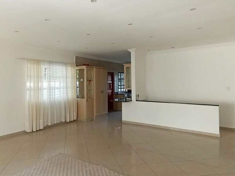 Spacious open-plan living area featuring neutral tiled flooring, recessed downlighting, and a partial wall divider leading into the kitchen space.