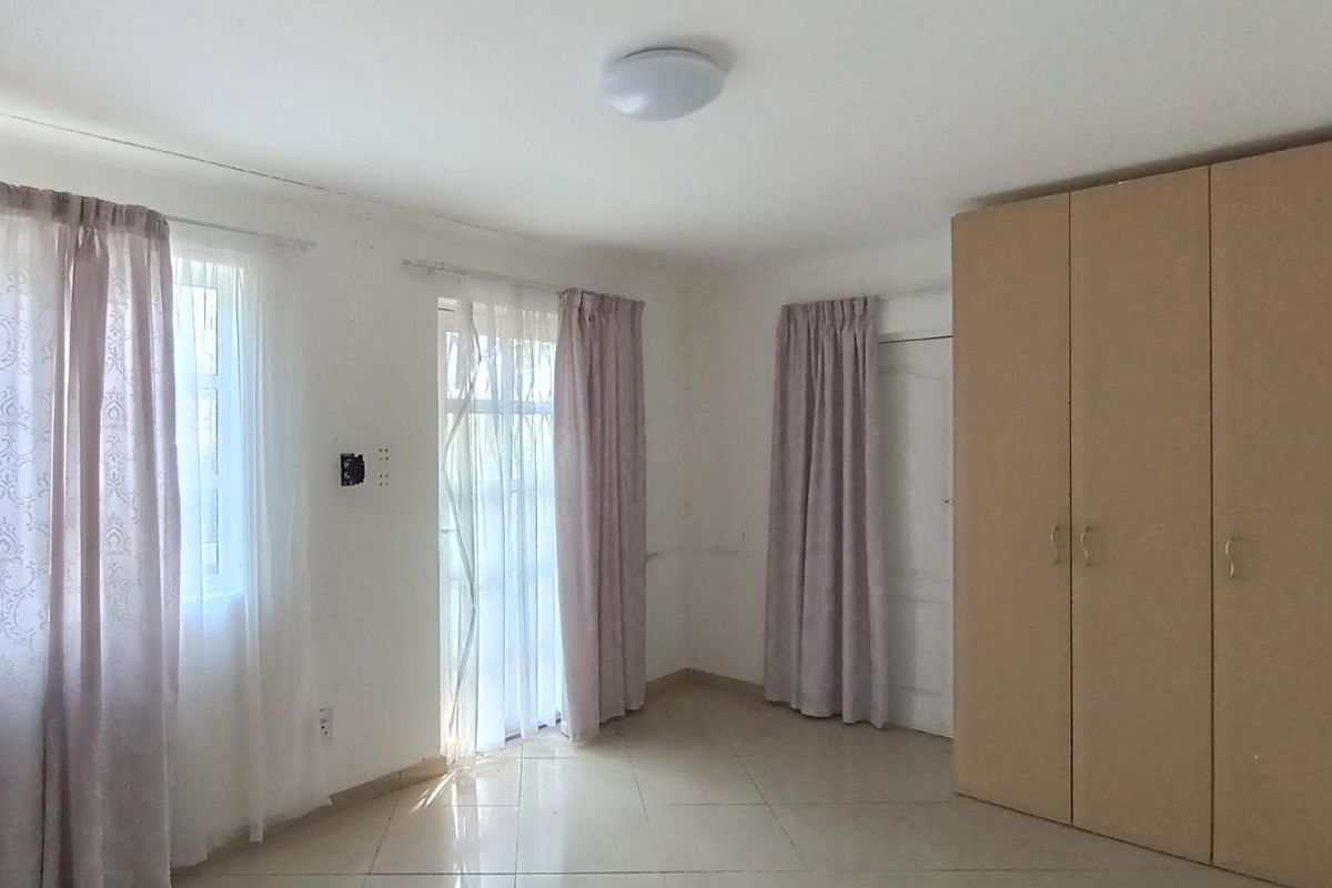 A bright, empty bedroom featuring tiled flooring, built-in cupboards, and direct access to an outdoor area through a glass door.