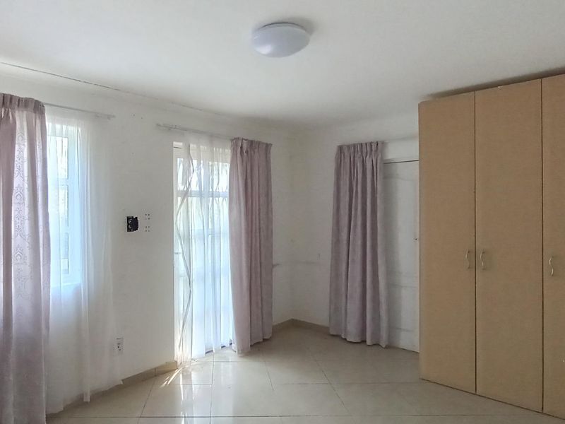 A bright, empty bedroom featuring tiled flooring, built-in cupboards, and direct access to an outdoor area through a glass door.