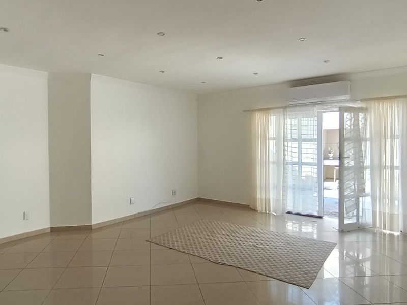 Spacious, light-filled living area featuring neutral tiled flooring, recessed lighting, and direct access to an outdoor space via a glass sliding door.