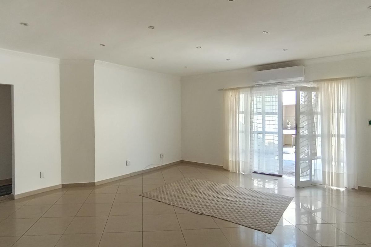 Spacious, light-filled living area featuring neutral tiled flooring, recessed lighting, and direct access to an outdoor space via a glass sliding door.