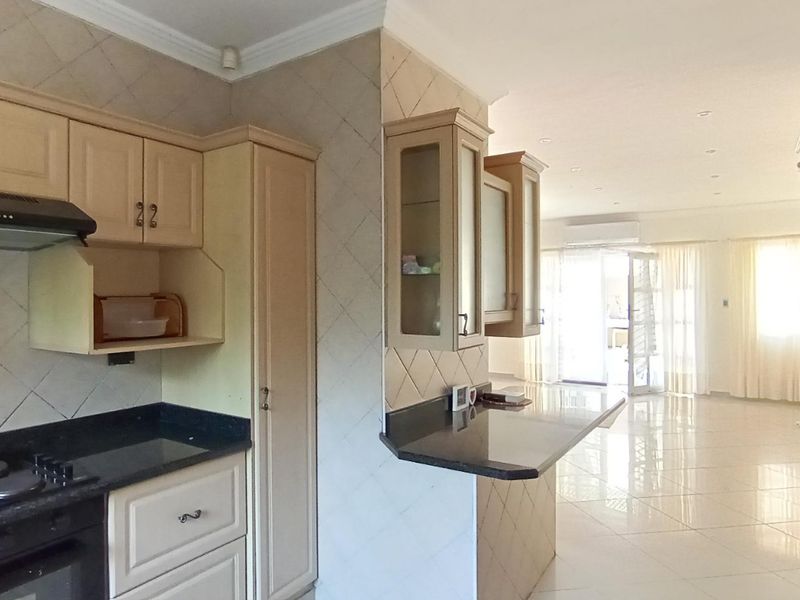 Open-plan kitchen featuring built-in cabinetry, granite countertops, and an electric hob, flowing into a bright, tiled living area with air conditioning.