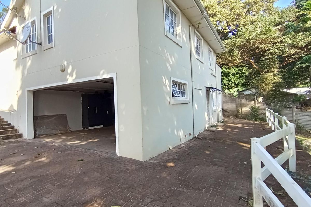 Rear exterior view of the townhouse featuring a paved driveway, garage access, concrete stairs, and a white picket fence boundary.
