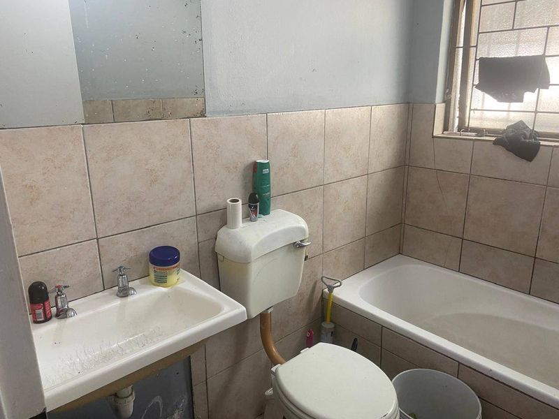A dated bathroom featuring a wall-mounted basin, standard toilet, and bathtub with tiled splashbacks, requiring cosmetic updates and maintenance.