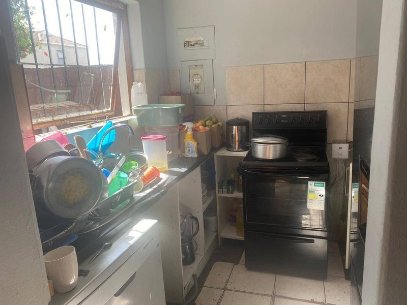 A compact kitchen featuring a freestanding stove, tiled splashback, and stainless steel sink, requiring cosmetic updates to improve functionality and aesthetic appeal.
