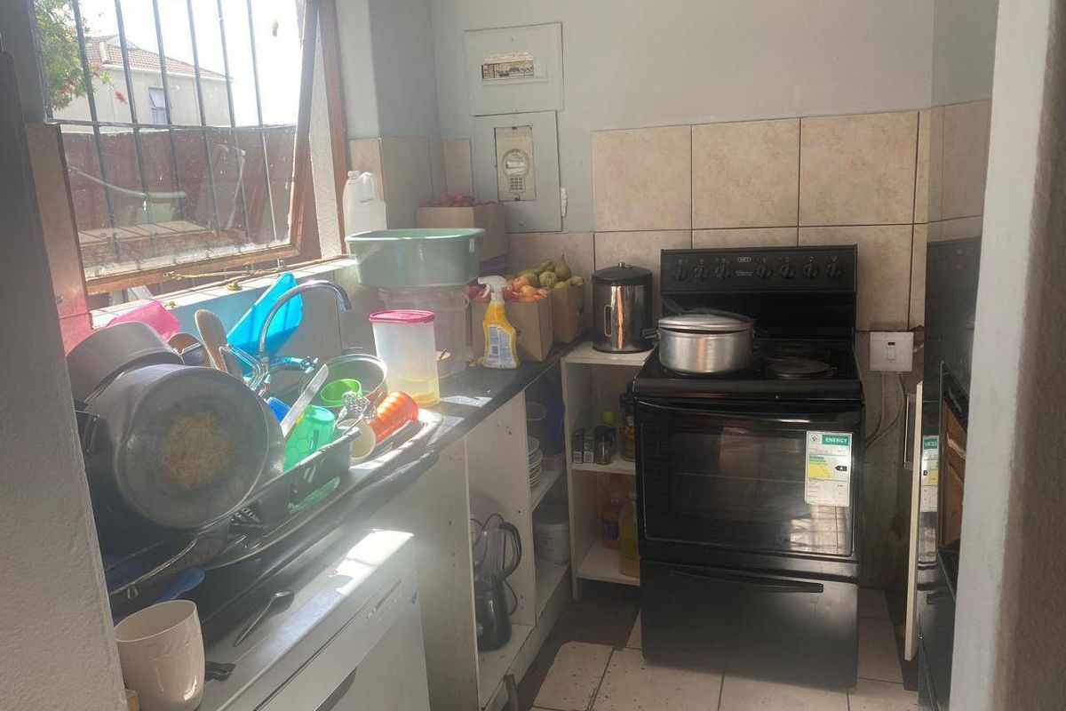 A compact kitchen featuring a freestanding stove, tiled splashback, and stainless steel sink, requiring cosmetic updates to improve functionality and aesthetic appeal.