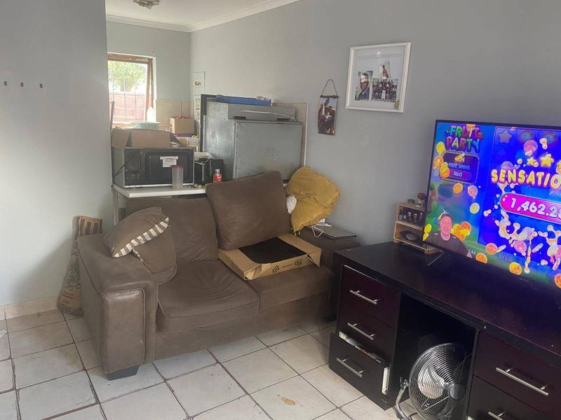 A living room area featuring ceramic floor tiles and coving, currently showing signs of wear and requiring maintenance to the flooring and wall finishes.