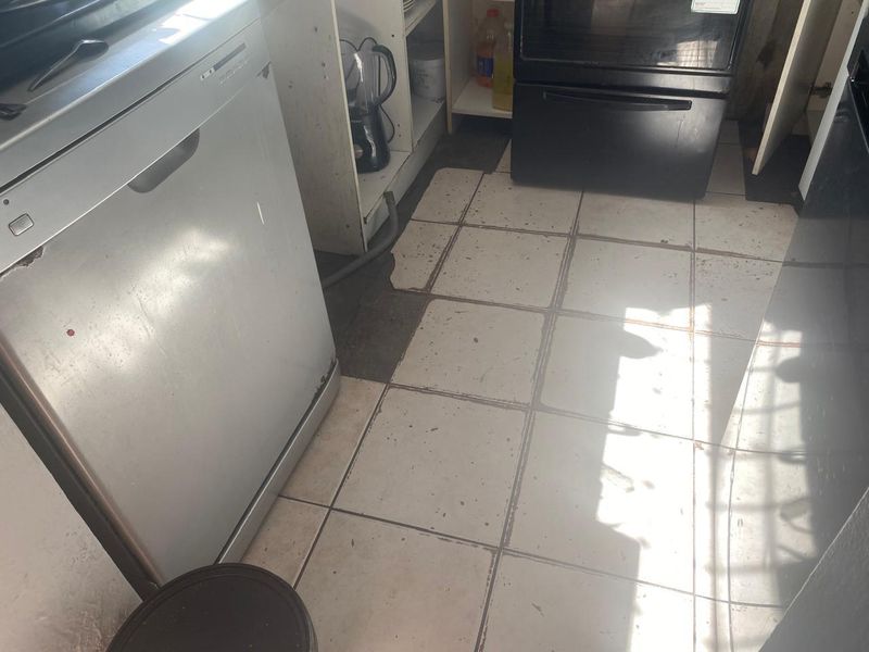 A kitchen area featuring built-in oven and cabinetry, currently showing significant wear to the tiled flooring and cabinetry finishes.