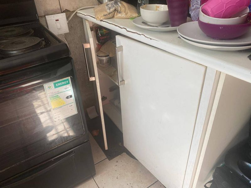 Close-up view of a kitchen area featuring a built-in oven, white cabinetry, and tiled flooring, showing signs of wear and damage to the countertop.