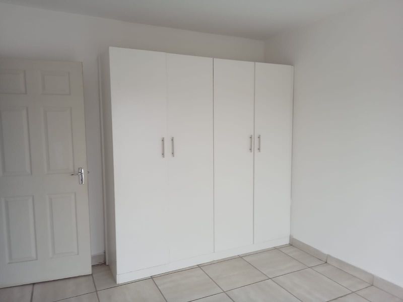 A clean, empty bedroom featuring neutral tiled flooring and a large, modern white built-in wardrobe.