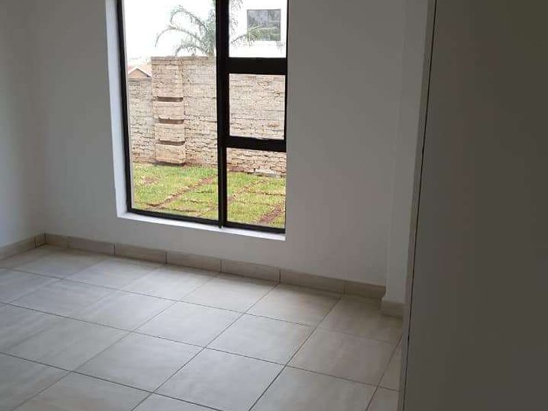 A bright, empty bedroom featuring neutral floor tiles, a modern aluminium window, and a built-in cupboard, offering a clean and versatile living space.