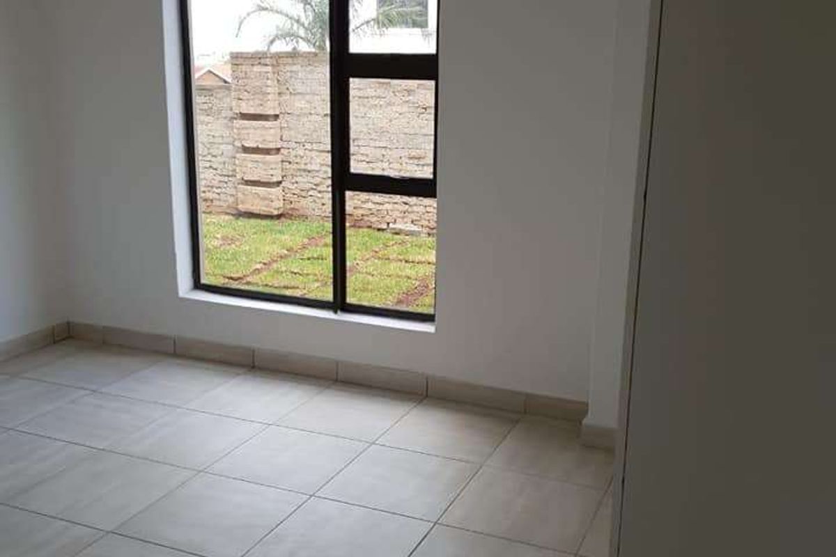 A bright, empty bedroom featuring neutral floor tiles, a modern aluminium window, and a built-in cupboard, offering a clean and versatile living space.