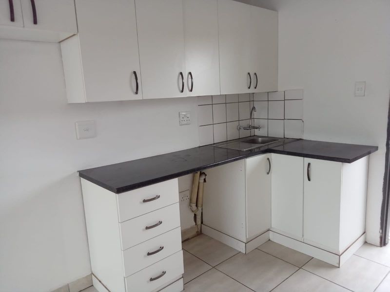 A compact kitchen featuring white cabinetry, dark laminate countertops, a stainless steel sink, and tiled flooring. The space is currently vacant.