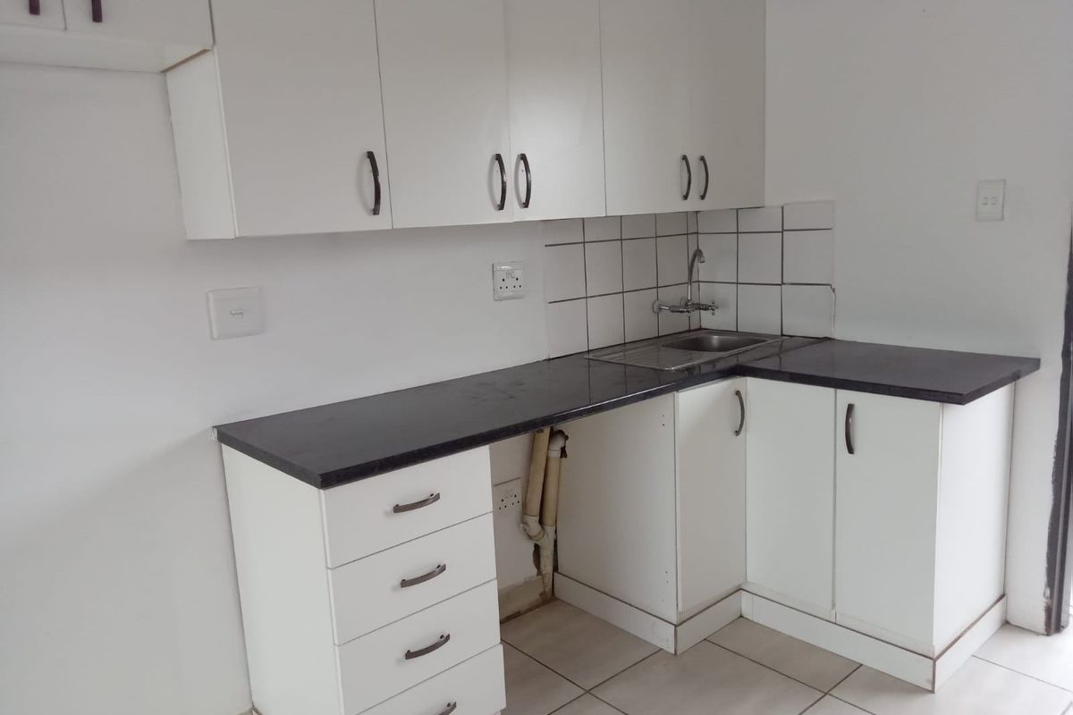 A compact kitchen featuring white cabinetry, dark laminate countertops, a stainless steel sink, and tiled flooring. The space is currently vacant.