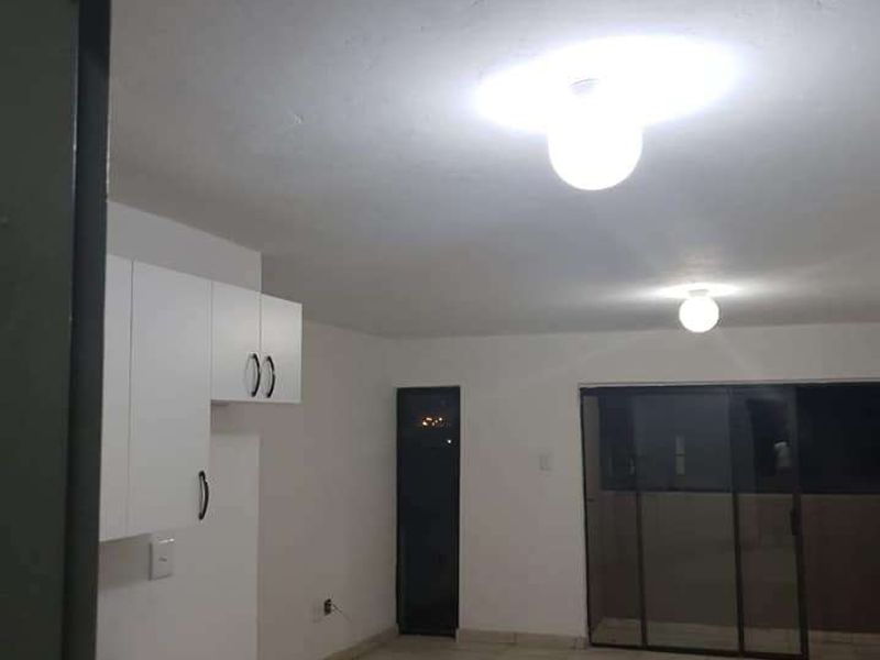 An open-plan living and kitchen area featuring tiled flooring, white built-in cabinetry, and a sliding glass door leading to an outdoor space.