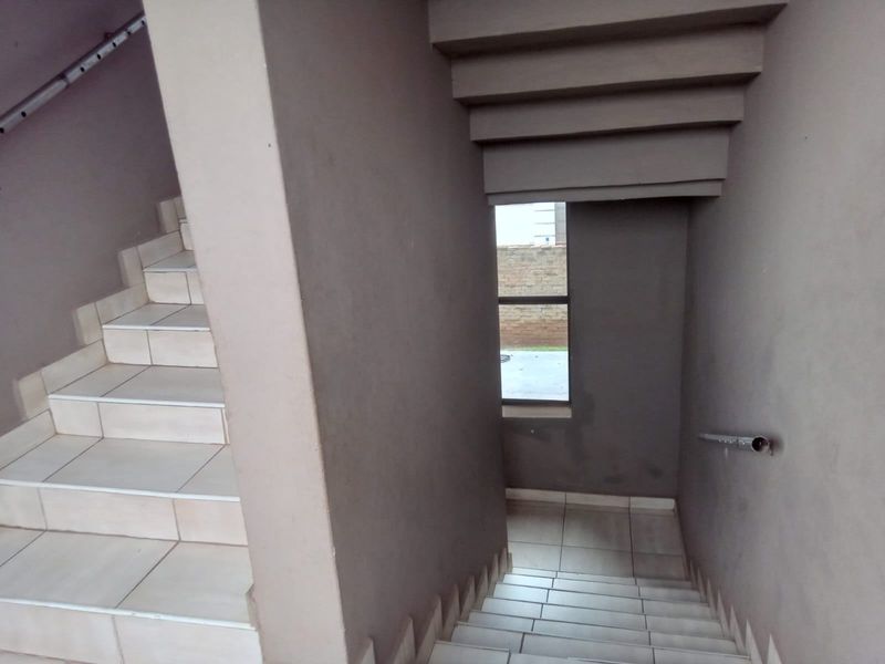 A tiled staircase with a metal handrail and a fixed window, showing signs of wear on the walls.