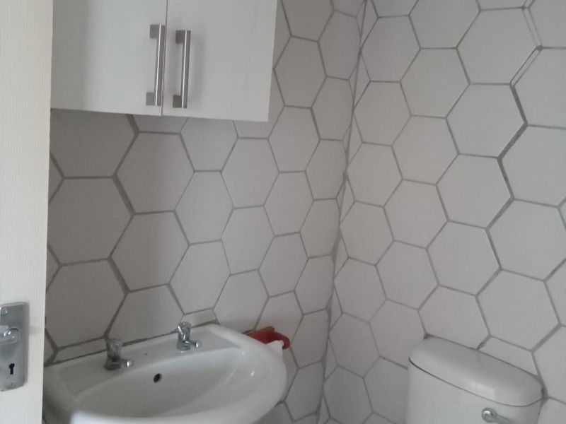 A compact bathroom featuring a pedestal basin, toilet, and modern white hexagonal wall tiling.