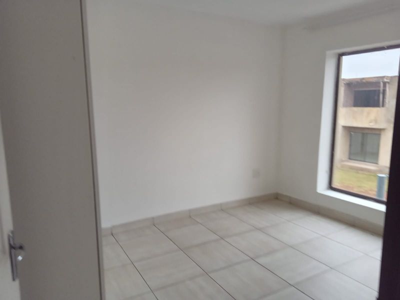 A bright, empty bedroom featuring neutral tiled flooring and a large window, providing a clean and versatile space ready for personalization.