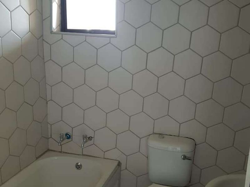 A functional bathroom featuring a bathtub, toilet, and pedestal basin, finished with modern hexagonal wall tiles.