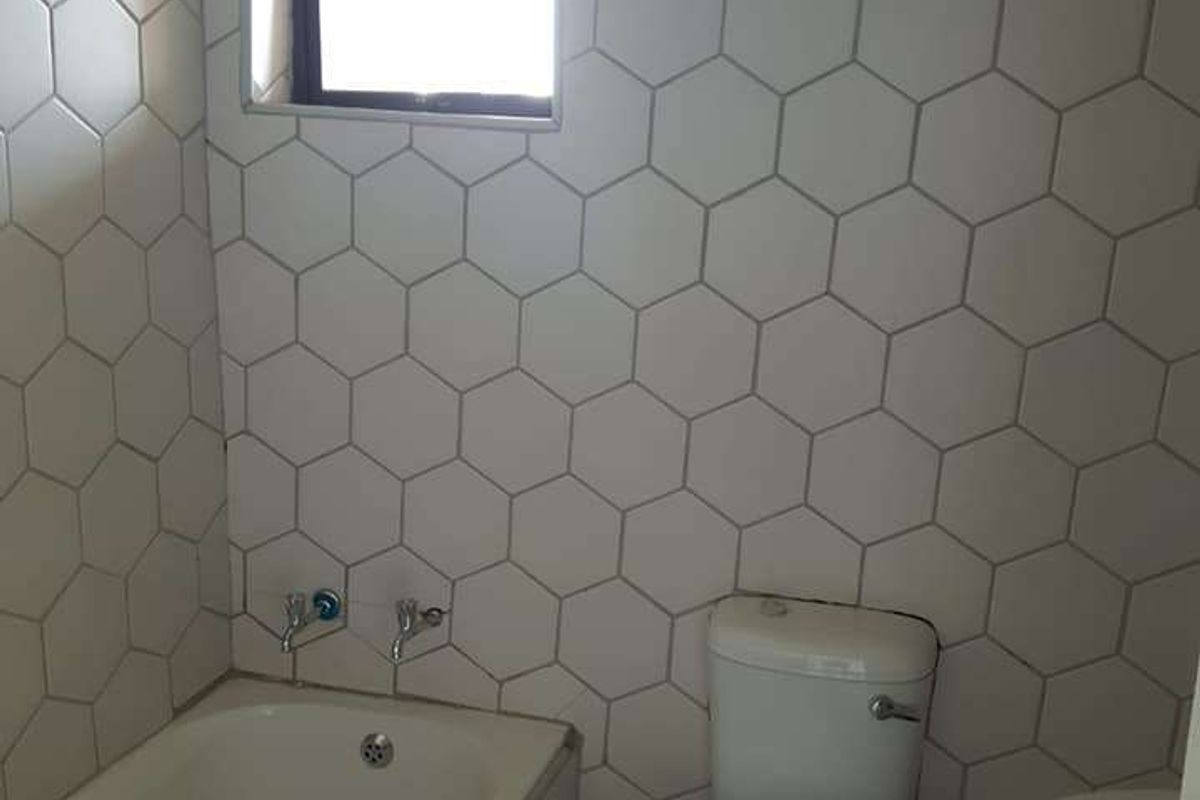 A functional bathroom featuring a bathtub, toilet, and pedestal basin, finished with modern hexagonal wall tiles.