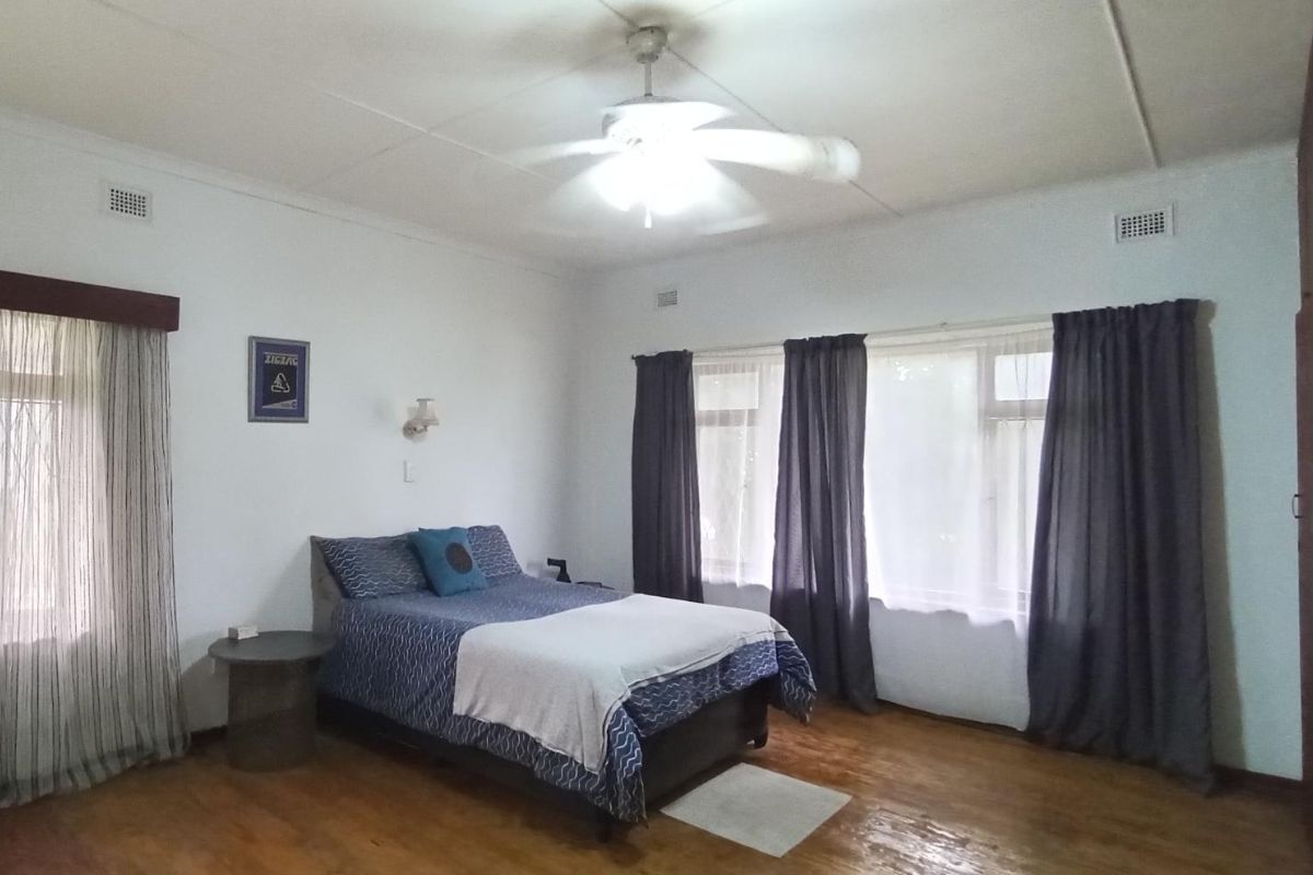 A spacious bedroom featuring timber flooring, a ceiling fan, and built-in storage cupboards with large windows allowing for natural light.