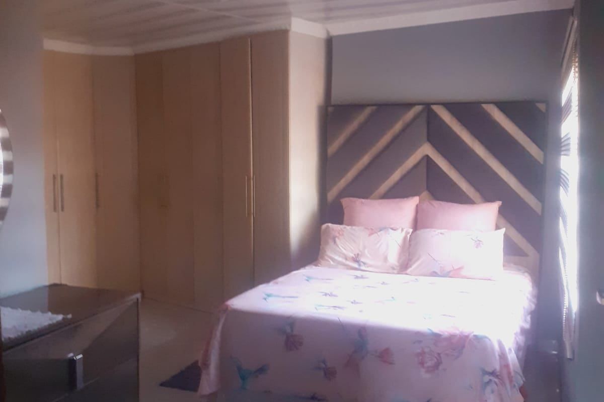 A bedroom featuring built-in cupboards, tiled flooring, and ceiling paneling, illuminated by natural light from the side window.