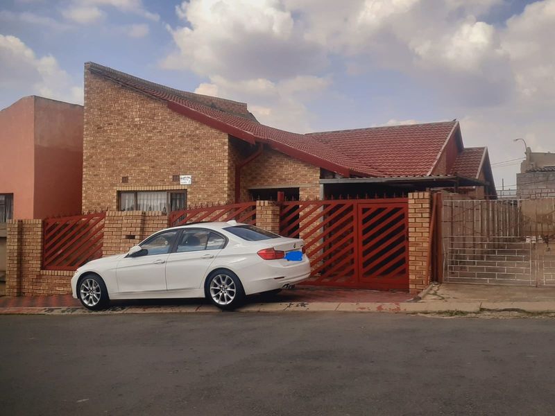 Front elevation of a face brick house featuring a pitched tiled roof, secure metal gate, and paved driveway area.