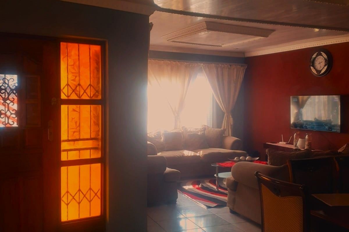 A living room featuring tiled flooring, decorative ceiling panels, and a timber-framed glass entrance door with warm natural light.