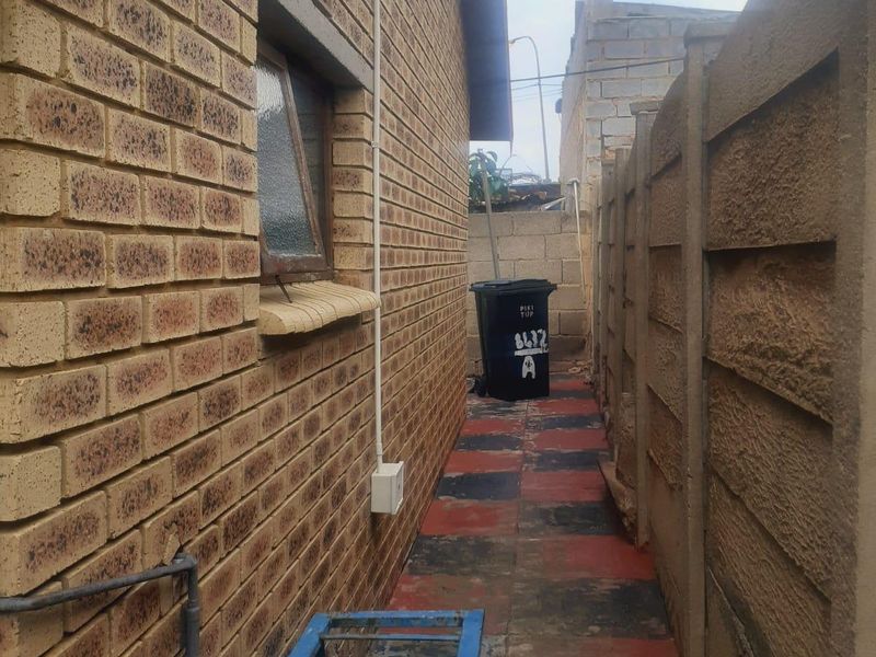 A narrow side passage featuring face brick exterior walls, a precast concrete boundary wall, and paved walkway.