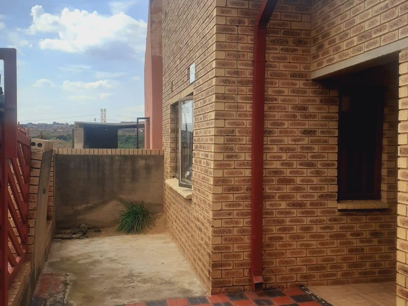 Rear exterior view of the property featuring a face brick facade and a paved patio area with a drainage downpipe.