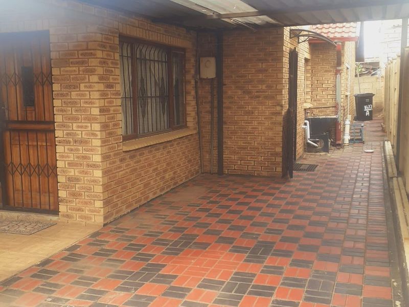 A paved side walkway and carport area featuring face brick walls, security gates, and functional drainage.