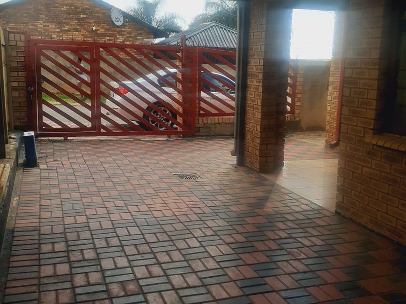 A covered carport area featuring brick pillars, paved flooring, and a secure metal gate entrance.