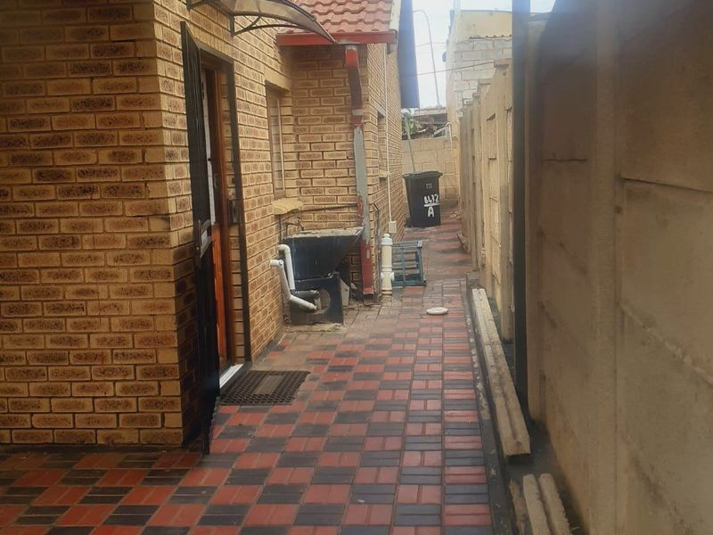 A side exterior walkway featuring brick wall construction, paved flooring, and a covered patio area leading to the rear of the property.