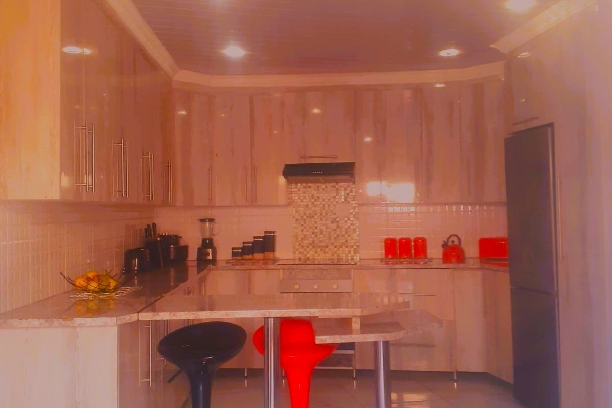 A modern kitchen featuring sleek built-in cabinetry, stone countertops, a tiled backsplash, and integrated appliances with a breakfast bar area.