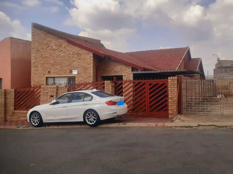 Front elevation of a face-brick house featuring a pitched tiled roof and secure gated entrance with perimeter walling.