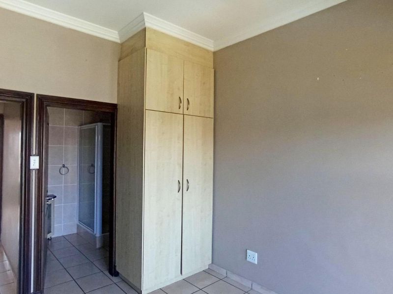 A bedroom featuring built-in cupboards, tiled flooring, and crown molding, with an adjacent bathroom visible through the doorway.